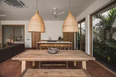 A long timber dining table under two woven pendants at Villa Kimilia