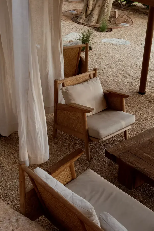 A cane and timber armchair with a linen cushion on the garden terrace at Under The Tree, Diriyah