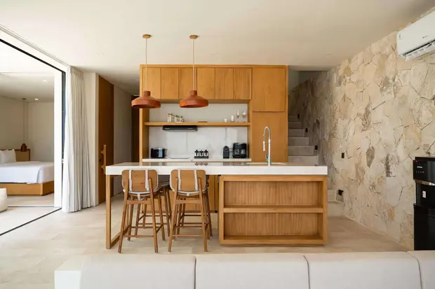 A timber kitchen island and stools against a stone wall at Ohana Villa