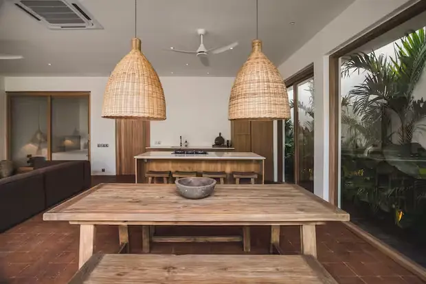 A long timber dining table under two woven pendants at Villa Kimilia